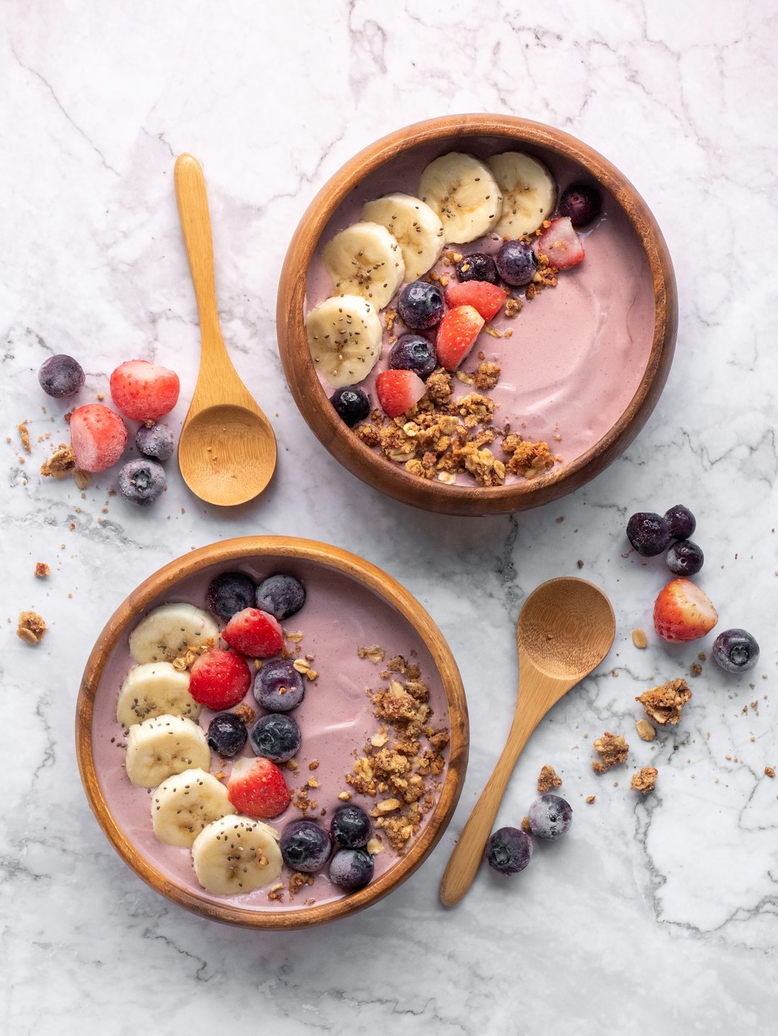 Two açaí bowls topped with banana, strawberries, blueberries and granola