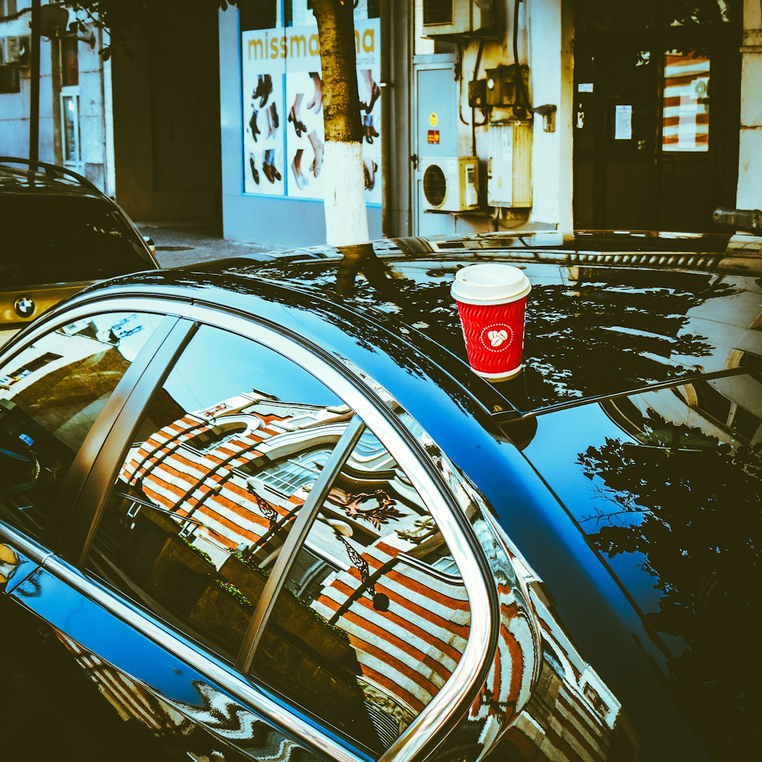A red takeaway coffee cup resting on the roof of a parked car
