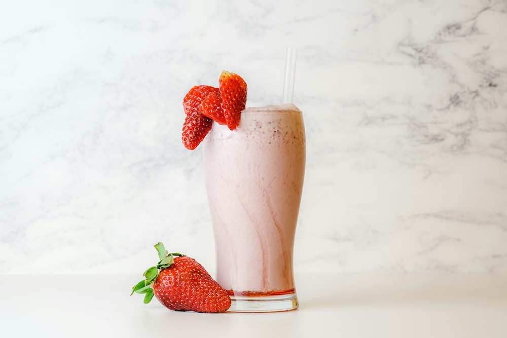 A strawberry shake in a tall glass with fresh strawberries